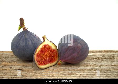 Figues mûres et pourpres sur une table en bois avec une fig. coupée en tranches sur un fond blanc Banque D'Images