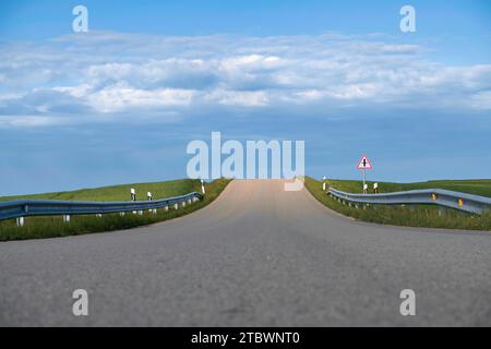Route asphaltée menant à travers des champs verdoyants dans une vue de recul dans un paysage rural pittoresque sous un ciel bleu avec des nuages Banque D'Images