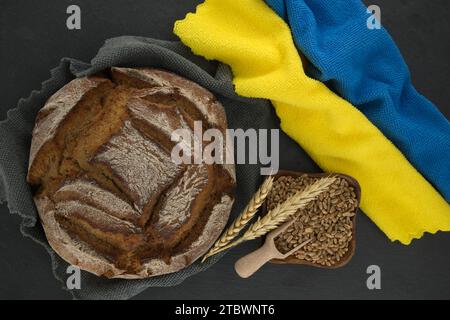 Pain de pain placé sur une table noire près du drapeau ukrainien couleurs bleu et jaune serviettes de cuisine et grain de blé, concept des exportations de céréales et global Banque D'Images