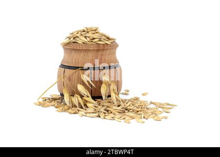 Tas de grains d'avoine biologique avec des coques ou des enveloppes dans un petit tonneau en bois isolé sur fond blanc. Grains d'avoine entiers avec enveloppe. Agriculture, alimentation Banque D'Images