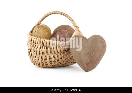 Pomme de terre en forme de coeur à côté d'un panier en osier avec des pommes de terre de différents types et couleurs isolées sur fond blanc Banque D'Images