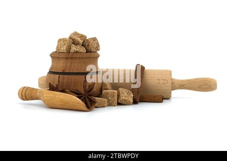 Faire dorer les cubes de sucre de canne dans un bol à sucre en bois à côté de bâtonnets de cannelle, d'anis étoilé et de punaise. Concept de confiserie isolé sur fond blanc Banque D'Images