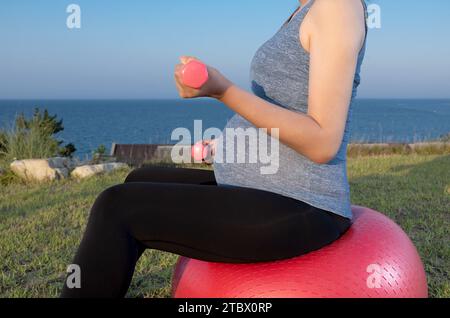 Une femme enceinte fait de l'exercice assise sur un ballon de gym à la plage Banque D'Images