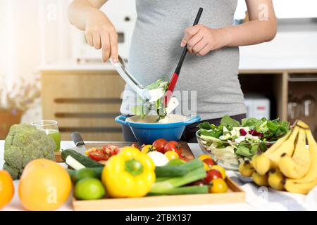 Une femme enceinte prépare un plat de salade à table Banque D'Images