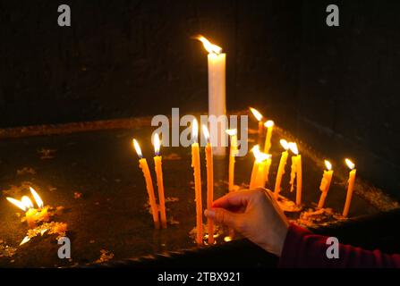 Main de femme plaçant la bougie allumée dans le stand de bougie votive à l'intérieur de l'église Banque D'Images