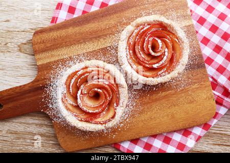 Paire de tartlets en forme de Mini Apple Rose saupoudrés de sucre en poudre sur une planche à pain en bois Banque D'Images