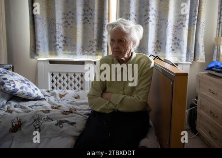 Une dame âgée de 80 ans est assise seule dans sa chambre à coucher de soins sociaux, Angleterre, Royaume-Uni Banque D'Images