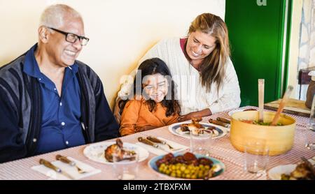 Heureuse enfant latine s'amusant à manger avec ses grands-parents à la maison Banque D'Images