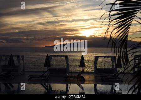 Magnifique coucher de soleil sur l'île de la Gomera vue de Los Gigantes sur Tenerife, avec chaises longues et palmiers en vue. Banque D'Images