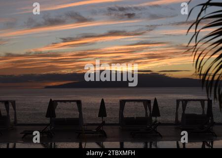 Magnifique coucher de soleil sur l'île de la Gomera vue de Los Gigantes sur Tenerife, avec chaises longues et palmiers en vue. Banque D'Images