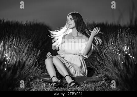 Ivano-Frankivsk, Ukraine 28 juillet 2023 : la jeune fille est assise sur l'herbe entre les rangées de lavande, les buissons de lavande et les fleurs sont illuminés par le grenier Banque D'Images