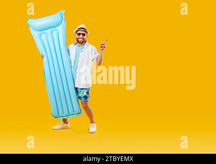 Homme joyeux avec matelas gonflable de natation pointant à l'espace de copie sur fond orange. Banque D'Images