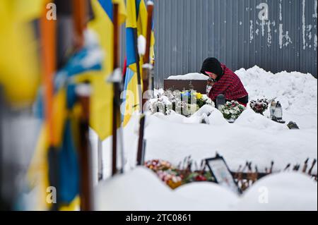 Non exclusive : LVIV, UKRAINE - 6 DÉCEMBRE 2023 - Une femme s'agenouille devant la tombe du cimetière Lychakiv lors d'une cérémonie en souvenir de la sienne Banque D'Images