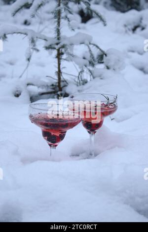 Deux verres de cocktail de champagne rosé avec des baies et du romarin sur une neige Banque D'Images