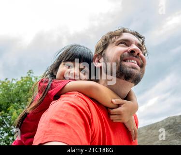 Latina fille et père. Son père lui donne un pigeon-back et elle regarde la caméra. Banque D'Images