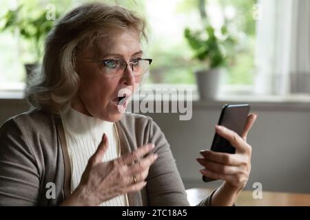 Femme âgée stupéfaite regarder sur l'écran de téléphone portable avec la bouche ouverte Banque D'Images
