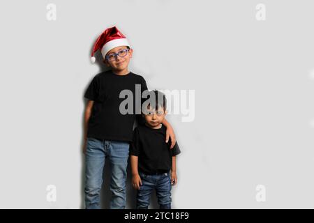 Enfants latinos à la peau foncée, frère aîné dans le chapeau de Santa prend soin de son jeune frère et passe du temps de qualité aux vacances pour célébrer Banque D'Images