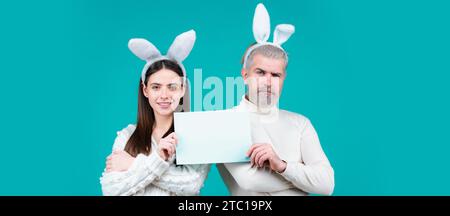 Le couple de Pâques tient un tableau blanc vierge pour votre texte.Bannière avec un couple de lapins drôle, espace de copie. Banque D'Images