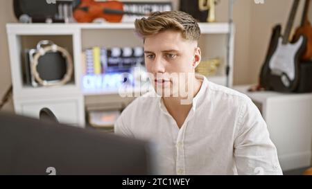 Jeune homme caucasien au visage sérieux se consacra à la création de chef-d'œuvre musical au studio de musique, en utilisant l'ordinateur comme instrument. Banque D'Images