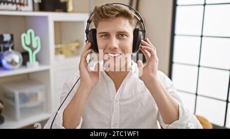 Beau jeune musicien caucasien, riant tout en écoutant avec confiance la mélodie évocatrice en studio de musique, immergé dans la magie musicale Banque D'Images