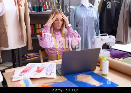 Jeune femme caucasienne couturière designer utilisant un ordinateur portable avec la main sur la tête, mal de tête parce que le stress. souffrir de migraine. Banque D'Images