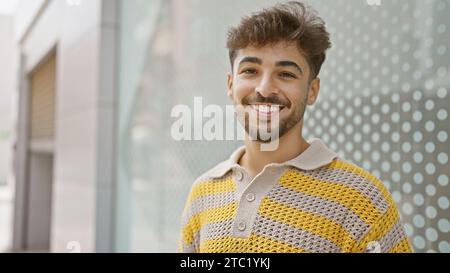 Jeune homme arabe confiant, appréciant joyeusement son temps à l'extérieur debout dans la rue de la ville, son visage barbu exprimant la joie pure et le bonheur à travers un Banque D'Images