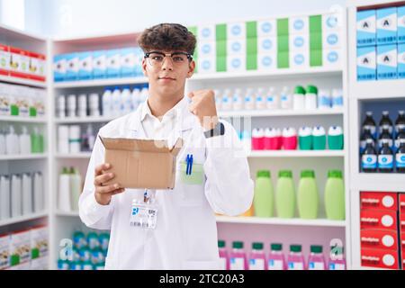 Adolescent hispanique travaillant à la pharmacie pharmacie tenant la boîte avec des pilules criant fier, célébrant la victoire et le succès très excité avec les bras levés Banque D'Images