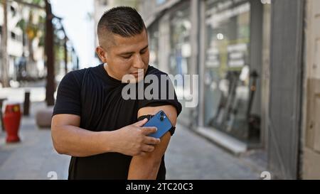 Jeune homme latin confiant, heureux scannant son capteur de diabète dans la rue de la ville à l'aide de son smartphone, surveillant de manière experte son taux de glucose, putti Banque D'Images
