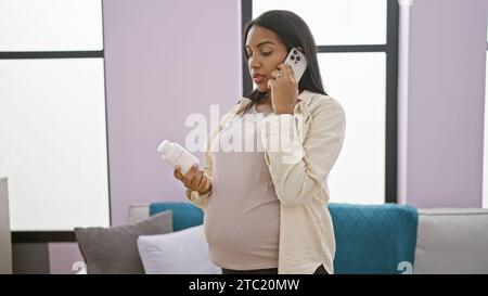 Inquiète jeune maman latine qui parle avec Medic de sa maladie par téléphone, tenant des pilules prescrites à l'intérieur dans un salon confortable Banque D'Images