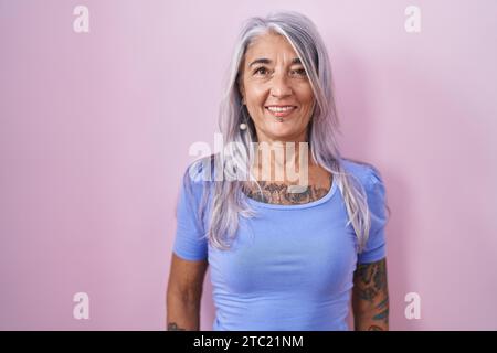 Femme d'âge moyen avec des tatouages debout sur fond rose avec un sourire heureux et cool sur le visage. personne chanceuse. Banque D'Images