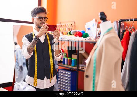Jeune homme hispanique sur mesure faire photo par smartphone à la veste à l'atelier Banque D'Images