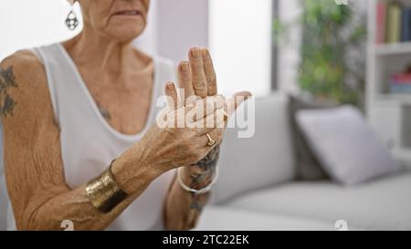 Femme âgée aux cheveux gris souffrant de douleurs intenses aux mains, assise dans le canapé du salon à la maison, femme âgée avec les cheveux courts semblant blessée, arthrose Banque D'Images