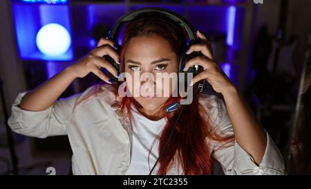 Streamer pour jeune femme rousse, plongé dans une séance de jeu intense, dans un jeu virtuel sérieux, casque allumé, encapsulé dans un éclairage tamisé Banque D'Images