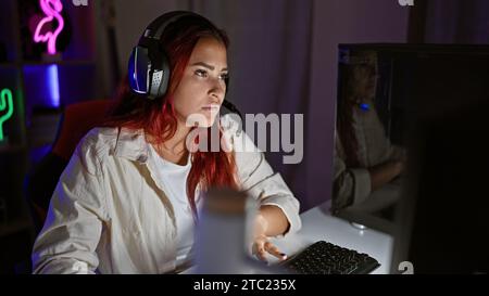 Streamer pour jeune femme rousse, plongé dans une séance de jeu intense, dans un jeu virtuel sérieux, casque allumé, encapsulé dans un éclairage tamisé Banque D'Images