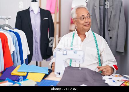 Homme d'âge moyen avec couturier gris utilisant la machine à coudre souriant regardant sur le côté et regardant loin la pensée. Banque D'Images