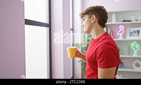 Attrayant jeune homme hispanique profondément absorbé dans la pensée, sirotant son café du matin, regardant par la fenêtre du salon à la maison, perdu dans Banque D'Images