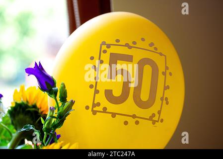 Un ballon avec un 50 imprimé dessus pour un 50e anniversaire avec un bouquet de fleurs sur le côté et devant une fenêtre Banque D'Images