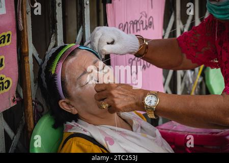 Bangkok, Thaïlande. 08 décembre 2023. Un gros plan d'un enfilage de visage avec un fil de coton, dans un salon de beauté de rue à Charoen Krung Road. Appelé « mang ming » en thaï, le filetage facial est une ancienne méthode d’épilation originaire de Chine, d’Inde et du monde arabe. La méthode utilise des fils de coton fins comme alternative à l'épilation à la cire ou à la épilation pour amincir les sourcils et éliminer les poils indésirables du visage. Crédit : SOPA Images Limited/Alamy Live News Banque D'Images