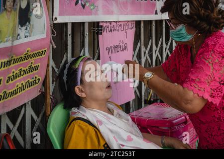 Bangkok, Thaïlande. 08 décembre 2023. Un membre du personnel d'un salon de beauté de rue est vu en train de filer le visage sur son client sur Charoen Krung Road. Appelé « mang ming » en thaï, le filetage facial est une ancienne méthode d’épilation originaire de Chine, d’Inde et du monde arabe. La méthode utilise des fils de coton fins comme alternative à l'épilation à la cire ou à la épilation pour amincir les sourcils et éliminer les poils indésirables du visage. Crédit : SOPA Images Limited/Alamy Live News Banque D'Images