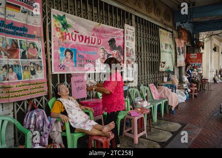 Bangkok, Thaïlande. 08 décembre 2023. Un membre du personnel d'un salon de beauté de rue est vu en train de filer le visage sur son client sur Charoen Krung Road. Appelé « mang ming » en thaï, le filetage facial est une ancienne méthode d’épilation originaire de Chine, d’Inde et du monde arabe. La méthode utilise des fils de coton fins comme alternative à l'épilation à la cire ou à la épilation pour amincir les sourcils et éliminer les poils indésirables du visage. (Photo Nathalie Jamois/SOPA Images/Sipa USA) crédit : SIPA USA/Alamy Live News Banque D'Images