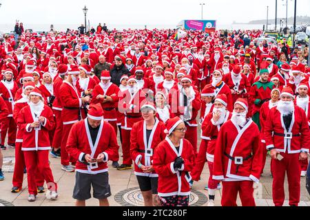 Plusieurs centaines de personnes toutes vêtues de vêtements rouges du Père Noël debout en plein air sur le front de mer à Herne Bay avant de prendre part à une course caritative, 'Santa's in the Bay' pour le Pilgrims Hospice. Banque D'Images
