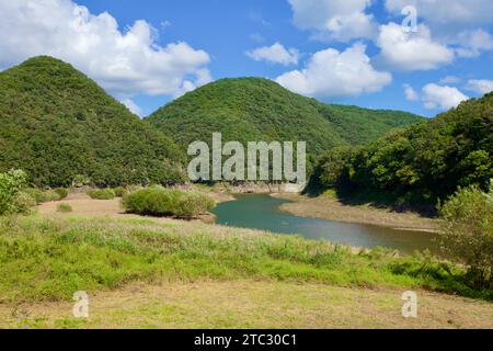 Un paysage pittoresque se déploie, avec des montagnes de forme conique, un ruisseau sinueux, et une étendue luxuriante d'arbres verts et d'herbe, offrant un sere Banque D'Images