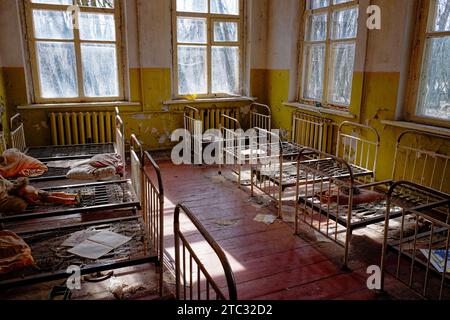 Une pièce négligée avec de la peinture jaune écaillée et un sol sale. Vieux lits d'enfants dans un jardin d'enfants abandonné. L'intérieur d'une pièce dans l'un des buil Banque D'Images