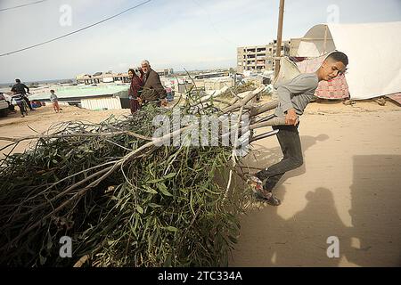 Khan Yunis, Gaza. 09 décembre 2023. Un garçon palestinien traînant du bois de chauffage pour des feux de camp alors qu’il marchait devant des tentes érigées par des Palestiniens déplacés par d’intenses bombardements israéliens sur la bande de Gaza dans des zones ouvertes près de la frontière égyptienne à Rafah, dans le sud de l’enclave palestinienne, le dimanche 10 décembre 2023., alors que les Palestiniens recourent aux alternatives les moins chères disponibles pour cuisiner et se chauffer dans un contexte de pénurie de ressources alors que les combats se poursuivent entre Israël et les militants palestiniens dans la bande de Gaza. Photo par Ismael Mohamad/UPI. Crédit : UPI/Alamy Live News Banque D'Images