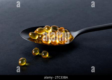 Capsules de gel jaune sur une cuillère noire studio nature morte Banque D'Images