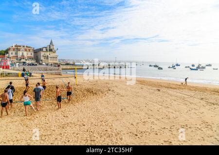 Un groupe de jeunes hommes et femmes actifs jouent au Beach volley dans le sable sur la plage de Praia da Ribeira à Cascais, Portugal. Banque D'Images