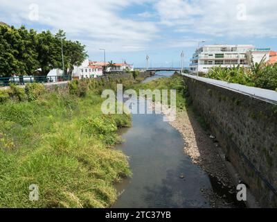 Machico, Madère, Portugal, 17 mai 2022 : vue de Ribeira de Machico, canal d'eau de la rivière au centre de la ville de Machico avec des arbres, des maisons et un pont Banque D'Images