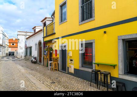 Un petit café trottoir peint en jaune vif avec tabourets de bar dans le centre historique de la station balnéaire de Cascais, Portugal. Banque D'Images