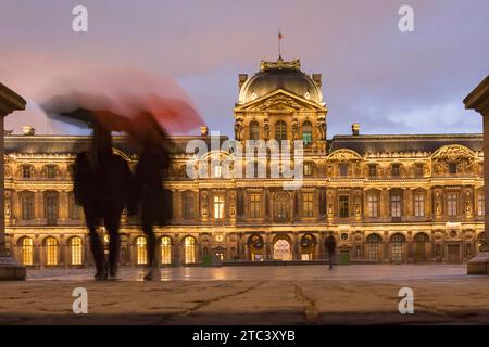 Place de la Cour, Musée du Louvre, Paris, France. Couple marchant sur la place de la cour pendant le coucher du soleil un jour de pluie. La façade du palais et la cour. Banque D'Images