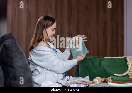 Femme enceinte pliant des vêtements de bébé assis sur le canapé à la maison. Banque D'Images